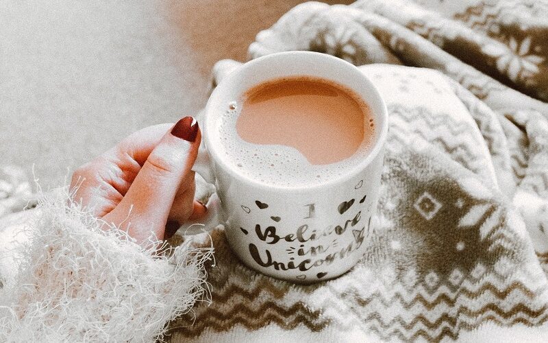 Lady sitting with a warm cup of tea and wrapped in a warm blanket