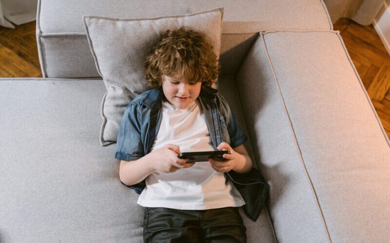 A Young Boy Lying on the Couch while Using His Phone