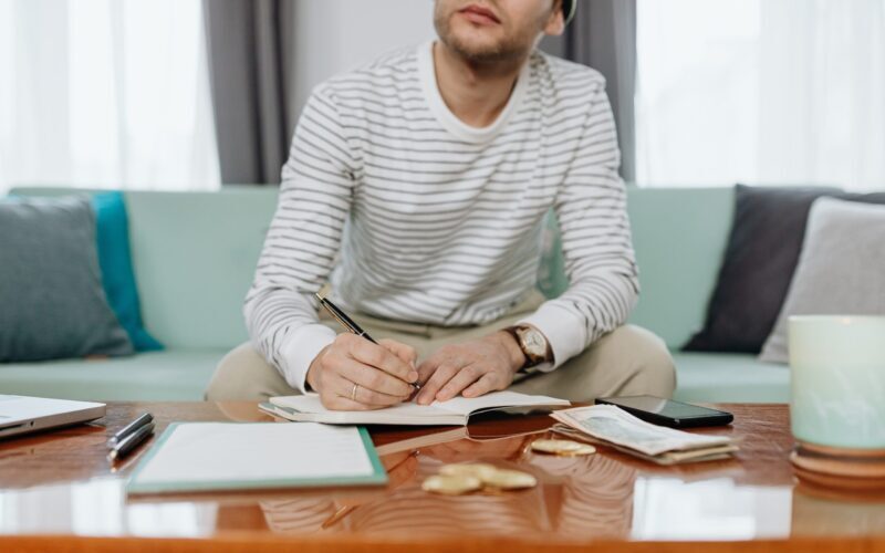 Man in White and Gray Striped Long Sleeve Shirt Sitting at the Table Doing Calculations