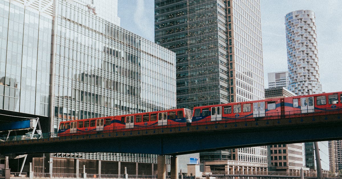 Saving money on train travel in UK - Red train crossing a bridge in front of Canary Wharf skyscrapers with river reflection.