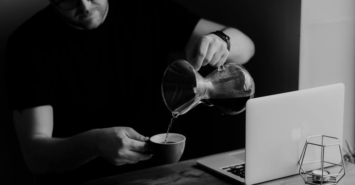 Side Hustles UK - Black and white image of a man pouring coffee next to a laptop.