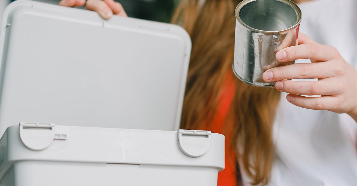 environmentally friendly money saving tips - Low angle of serious female with long hair putting tin can into opened bucket for metal trash