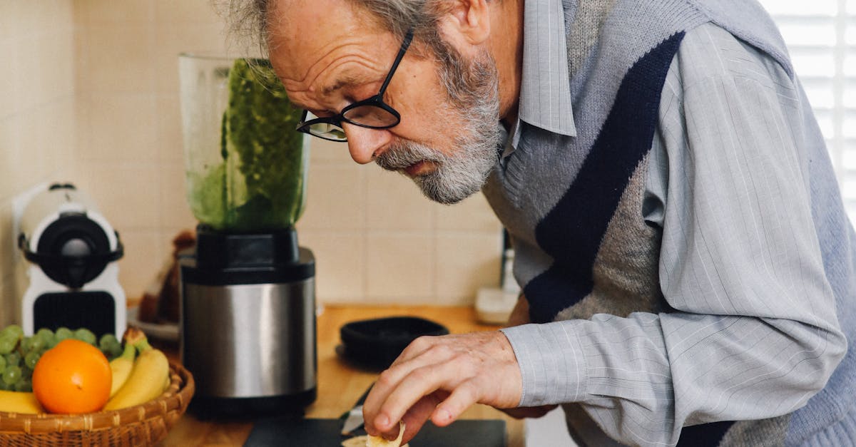 green energy tariff - Elderly man making a healthy green smoothie in a kitchen with fresh fruits.