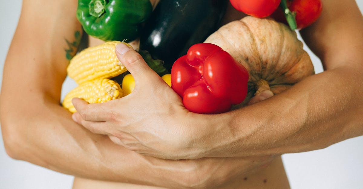 Affordable Gourmet Dining - A man's torso holding a variety of fresh vegetables including peppers and corn.