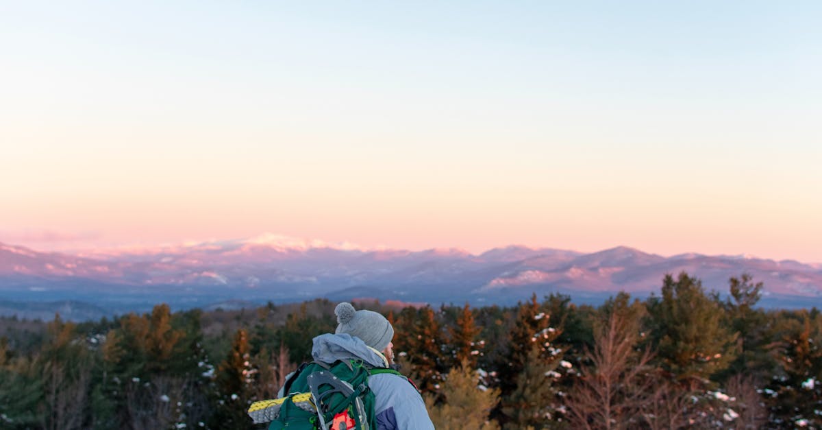 Affordable World Travelling - A backpacker overlooks snow-covered mountains during a vibrant winter sunset in Lincoln, New Hampshire.