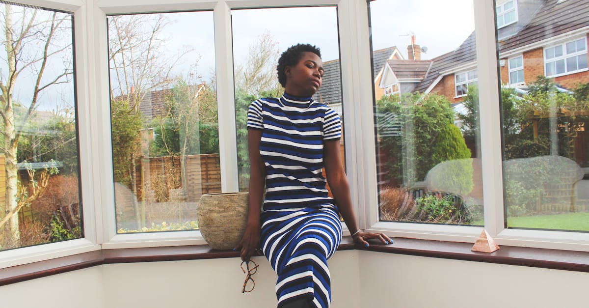 frugal living in the UK - Stylish portrait of an elegant woman in a striped dress sitting by a window.