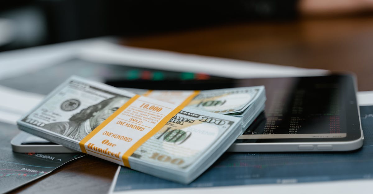 Cash ISAs - A stack of $100 bills placed on a tablet displaying financial graphs, representing modern finance.