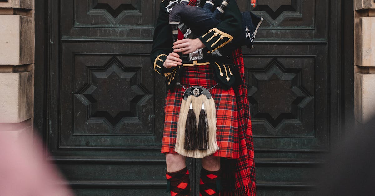 saving money at music festivals - A traditional Scottish bagpiper in vibrant tartan attire stands before an ornate door in Edinburgh, Scotland.