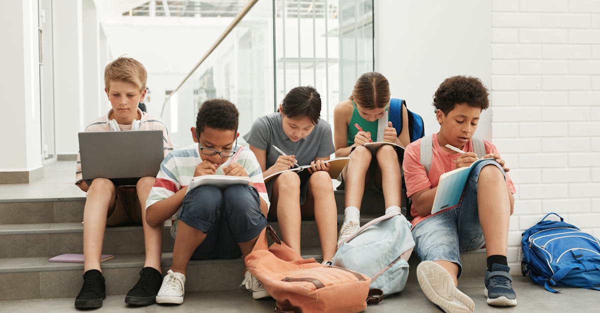 saving on university textbooks - A group of school students sitting in a hallway, focused on studying and writing.