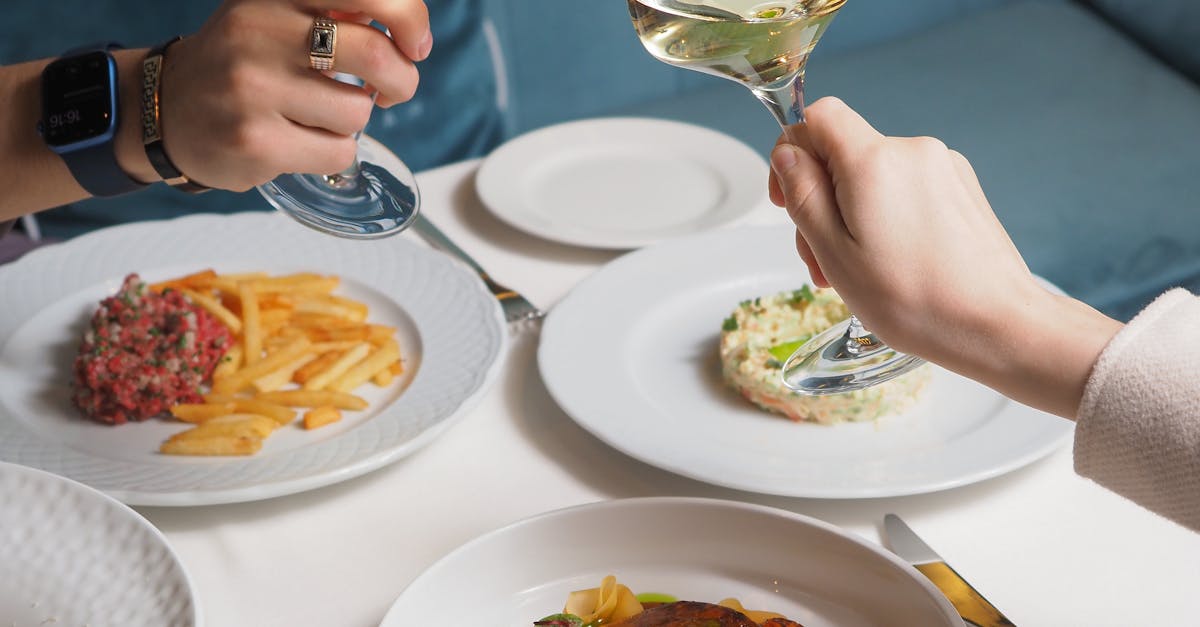 Affordable Gourmet Experiences - Two people toasting wine glasses over a gourmet meal in a luxurious setting.