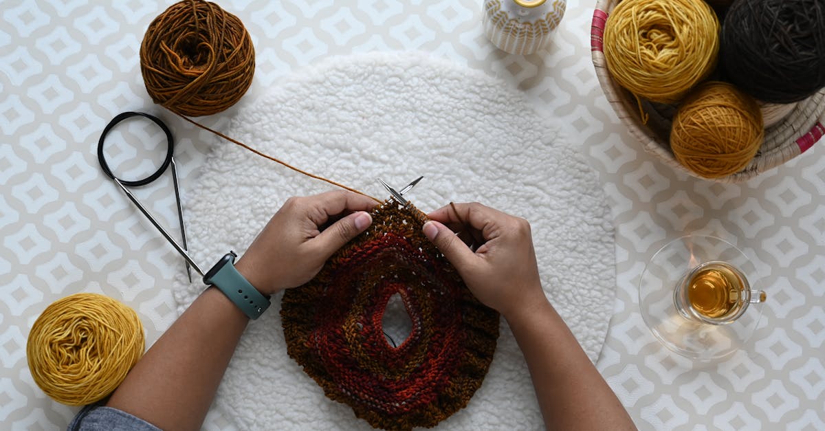Upcycling for Profit in the UK - Overhead view of hands knitting with vibrant yarns on a geometric patterned blanket.