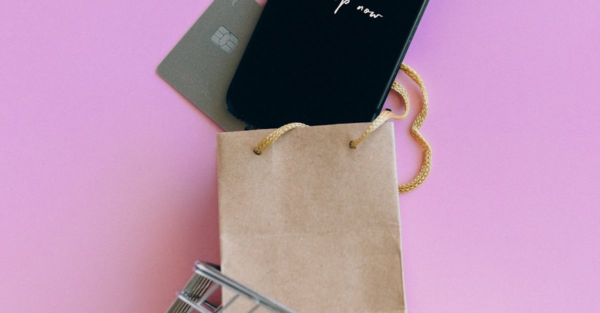 Buy Now Pay Later UK - A smartphone, credit card, and bag in a miniature shopping cart on a pink background.